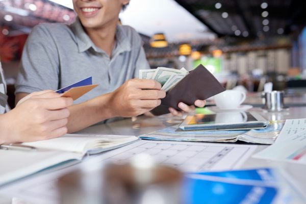Smiling young man and his wife counting money while planning vacation trip to Europe, blurred background