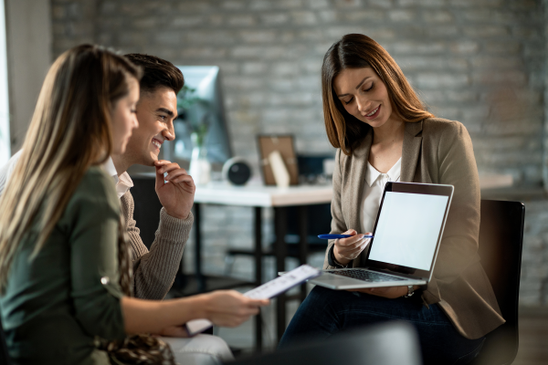 smiling-real-estate-agent-using-computer-while-having-meeting-with-young-couple-making-investment-plans